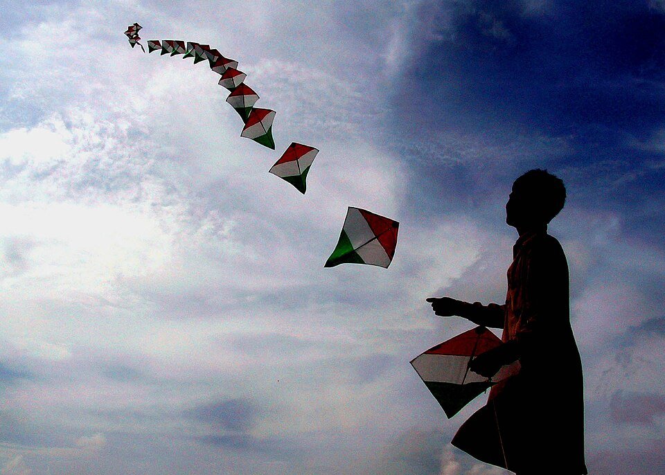 Boy holding a diamond kite while a train of kites flies above