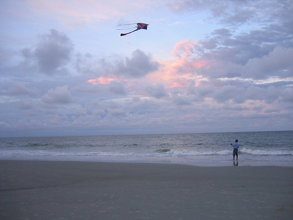 Person flying a kite on an open beach at dusk